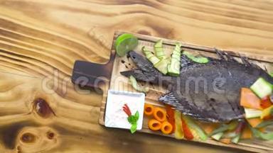 烤鱼和蔬菜装饰在烧烤餐厅。 食物成分：蔬菜和香料烤鱼